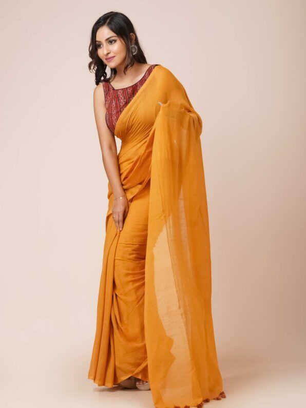 A woman showcasing a mustard yellow mul cotton saree with tassel details along the border. The saree is lightweight, breathable, and perfect for casual or daily wear.